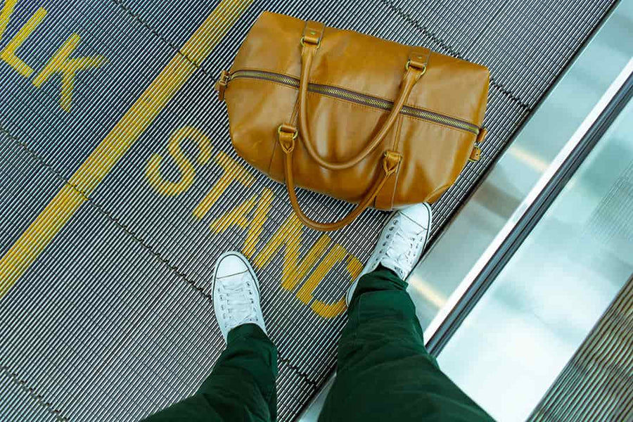 A flight passenger with luggage on a moving walkway at the airport.