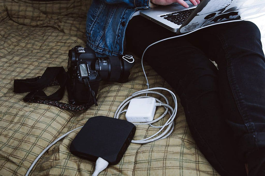 A photographer using an Omni charger for their laptop while their camera sits next to them