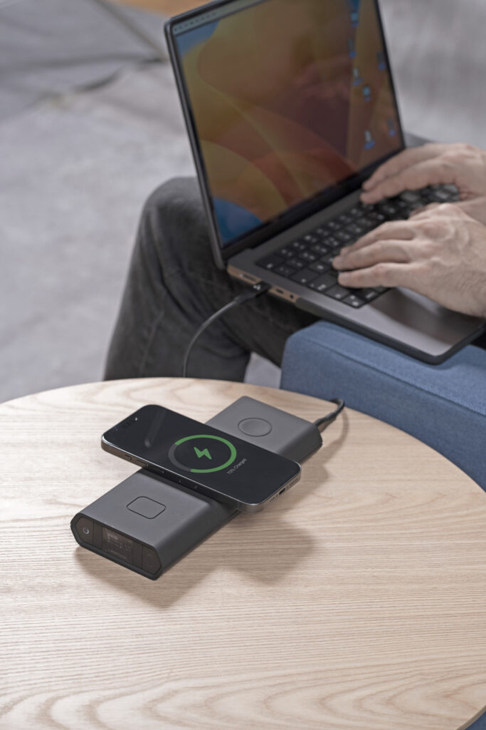Omni power bank wirelessly charging a phone beside a laptop