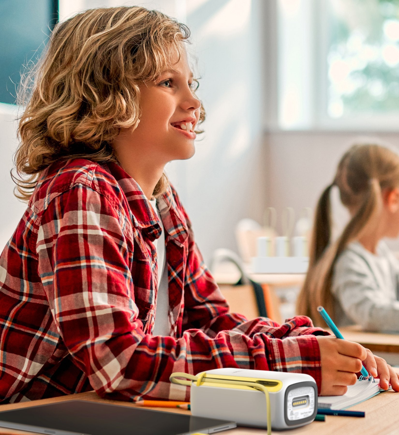 Student smiling at her classroom desk with an Omni Locker 10E unit beside her tablet
